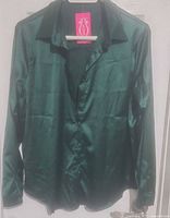 Front view of emerald green blouse on hanger with tag attached