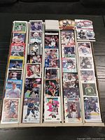 Photo showing front face of various sports cards from different sports, arranged in several rows inside a box, featuring hockey, basketball, football, and baseball cards.
