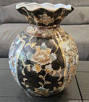 Oblique front view of hand-painted Satsuma vase showing detailed floral designs with gold accents on black background.