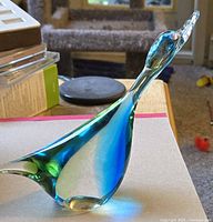 Clear view of the blue and green art glass bird figurine showing its shape, color, and size relative to surrounding objects.