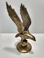 Solid brass eagle figure with detailed wings spread, perched on globe and round base, photographed on plain background.