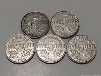 Five 1922 Canadian nickel five-cent coins arranged with the reverse side up, showing denomination and maple leaves.