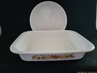 Top view showing rectangular Corning Ware casserole pan with floral side design and round white ceramic dish behind it, showing baking surface area.