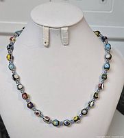 Full view of colourful glass beaded necklace displayed on a white bust stand showing alternating patterned beads in multiple colors.
