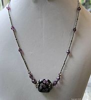 Full view of the necklace on a display bust showing silver-toned chain with purple beads and floral glass pendant.