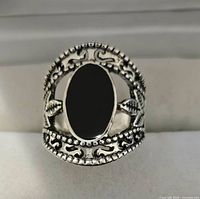 Front view of silver toned ring showing black oval stone and detailed band design.