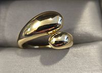 Clear close-up of gold toned ring showing smooth shiny surface with two rounded ends, sitting on a neutral background.