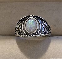 Front view of silver toned ring displaying oval opalescent center stone with detailed decorative band