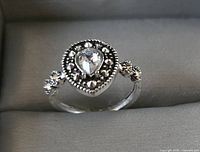 Front view of the silver-tone fashion ring with pear-shaped white stone centerpiece and bead accents on band.