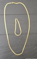 Photo showing a gold plated necklace and matching bracelet laid flat on a dark wood surface.