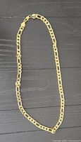 Gold plated heavy chain link necklace laid flat on a black wood grain surface showing entire length and clasp.