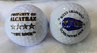 Close-up photo showing both golf balls side by side, highlighting the Property of Alcatraz, 'The Rock', label and the San Francisco Country Club logo with cable car illustration.