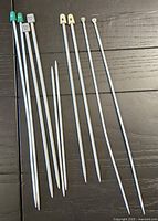 Five pairs of knitting needles in various sizes and colors laid out on a dark wooden surface.