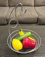 Metal wire basket holding four colorful glass fruit and vegetable figurines on dark table