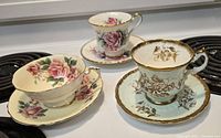 Three Paragon teacup and saucer sets displayed together showing floral and gold designs.