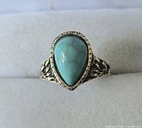 Top-down view of silver toned ring with pear-shaped turquoise colored stone mounted in textured band.