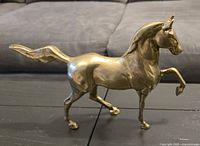 Side view of brass horse figurine showing right side with tail flowing back and right foreleg raised.