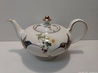 Side view of the porcelain white tea pot with hummingbird design, showing spout, handle, and floral painting details.