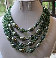 Close-up front view of the necklace showing the four strands of faceted and oval green beads with iridescent highlights.