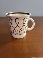 Side angle view of the demitasse cup showing looped brown pattern with dots and solid brown rim band, handle visible
