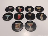 Top view of all 10 round metal drink coasters showing colorful cocktail illustrations on black backgrounds.