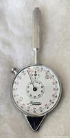 Vintage Minerva Opisometer with round dial and grooved handle against light background.