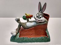 Front and side view of Bugs Bunny pencil holder showing character reclining on tree stump and pencil compartment at back.