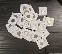 A pile of 40+ collectible world coins in white cardboard protective sleeves with handwritten notes indicating country and year.