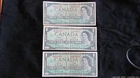 Front view of the three 1967 Canadian Centennial one dollar notes, showing Queen Elizabeth II portrait and serial numbers, signed by Beatty-Rasminsky, in used condition.