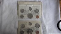 Top-down view of two sets of Canadian coins in sealed plastic sleeves with paper backings, showing six coins in each set including a penny