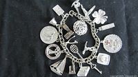 Close-up photo of sterling silver charm bracelet showing various charms attached including a thistle, tennis racket, and more.