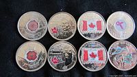 Top side of 10 commemorative Canadian quarters showing colored commemorative designs including poppies, breast cancer ribbon, maple leaf, Canadian flag, and animal motifs.