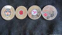 Photo showing the front faces of four coloured Canadian coins: 2020 Toonie with Haida grizzly bear, 2008 poppy quarter, 2006 breast cancer ribbon quarter, 2012 maple leaf Tecumseh quarter.