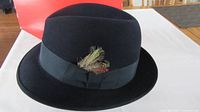Close-up view of black felt fedora hat with black ribbon band and feather detail