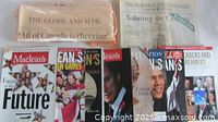 Photo shows unopened Globe and Mail newspaper, Kingston Whig-Standard Millennium Edition, and multiple Maclean's magazines with various covers including the Olympic Hockey story and commemorative issues.