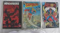 Front view of all three comics showing covers: Ronin Book One 1983 hardcover, Supergirl No.1, Arion No.1 in protective sleeves lying side by side on white cloth.