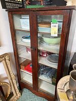 Front view of antique pine wood cupboard with glass doors, containing plates and bowls (not included in lot). Metal latch is visible.