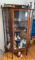 Full view of the solid oak antique china cabinet with curved glass panels displaying various small decorative items inside.
