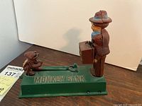 Side view of antique mechanical monkey bank showing man with briefcase and monkey figure on green base marked MONKEY BANK.