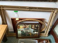 Photo showing the large ornate rectangular gold frame, medium brown rectangular frame, smaller oval gold frame and the antique oak mirror with rounded top corners placed in front, all leaning against a wall.