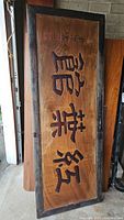 Full length of large rectangular wooden sign with dark carved Japanese characters and worn frame.