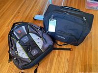 Photo showing Swiss Army backpack and black rolling carry-on bag placed on wooden floor