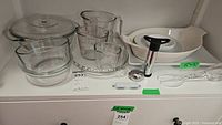 Wide view of glass baking dishes, measuring cups, and kitchen utensils arranged on a white shelf