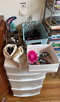 Wide view of plastic storage drawers topped with multiple containers holding assorted sunglasses, children's accessories, nail products, and trinkets. Two decorative ornaments partially visible on top of the organizer.