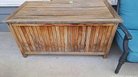 Front view of teak storage box showing weathered wood and damage.