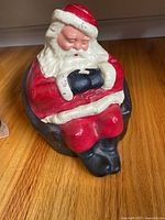 Front angle of sleeping Santa Claus bank showing painted red suit, white beard, and black gloves and boots.