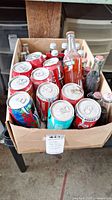Box with multiple collectible aluminum cans, mostly Coca-Cola with one other colorful can and one turquoise can