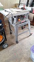 Photo showing full view of Craftsman table saw on metal stand with wheels, power cord visible, located in garage area.