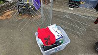 Plastic bin containing dog sweater, blanket, and other pet accessories seen within the metal dog pen