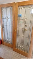 Pair of two wooden framed French doors with decorative clear glass panels showing geometric leaded designs and brass-colored knobs